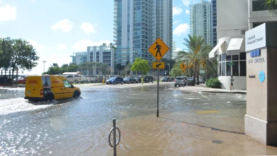 A van drives through a fair-weather flood durin' the mornin' high tide on a sunny day in October 2016 in downtown Miami